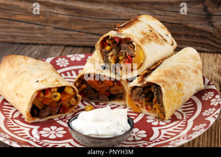 Burrito si avvolge con manzo e verdure su sfondo di legno. Burrito di carne bovina, cibo messicano. Foto Stock