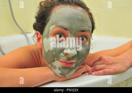 Volto di donna giovane con maschera di fango nella vasca da bagno. Foto Stock