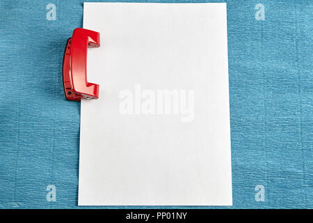 Ufficio rosso punzone con foglio di carta bianco, sfondo blu. Foto Stock