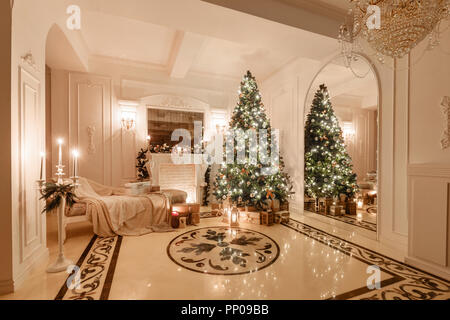 Interni classici di una camera bianca. Serata di Natale a lume di candela. appartamenti classic con un caminetto bianco, albero di Natale decorato, divano letto, grandi finestre e un lampadario. Foto Stock