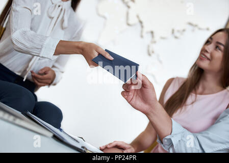 Agente di viaggio e coppia giovane. Giovane donna sorridente e dando i biglietti, passaporto con visto per turisti. Agenzia di viaggi ufficio interno con grande mappa del mondo in backgrownd Foto Stock