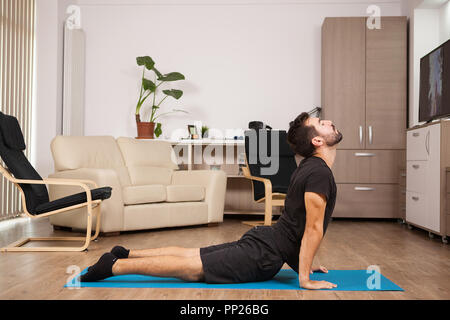 I giovani adulti facendo yoga cobra pongono sulla sua casa piano. Home te Foto Stock