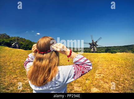 Bella ragazza ucraina indossando ghirlanda di fiori in legno mulini a vento a sfondo etnico bianco shirt all'architettura nazionale museo di Pirogovo. Kiev Foto Stock