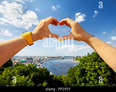 Donna mani in forma di cuore con giallo guarda contro il panorama della città di Kiev downtown in Ucraina Foto Stock