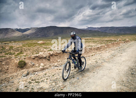 Uomo in mountain bike sulla strada del paese di montagna a cielo tempestoso sfondo. Foto Stock
