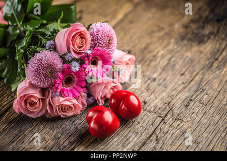 Bouquet di fiori con due cuori rossi su un tavolo di legno. Foto Stock