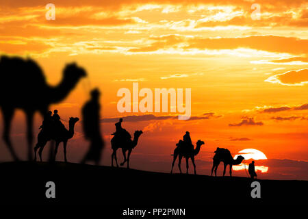 Caravan a piedi con cammello attraverso il deserto di Thar in India, mostrano silhouette e drammatico sky Foto Stock