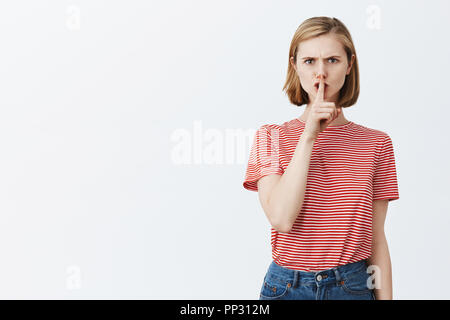 Pretendo di essere rinchiusi. Arrabbiato e dispiaciuto rigorosa sorella maggiore con taglio di capelli biondi, accigliata e shushing, dicendo shh e rendendo shush gesto con il dito indice sulla bocca, chiedendo di tacere Foto Stock