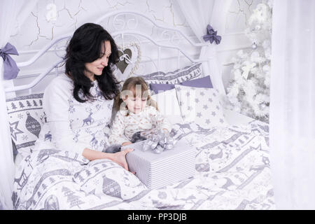 Madre dà un regalo per un bambino nel letto alla vigilia di Natale Foto Stock