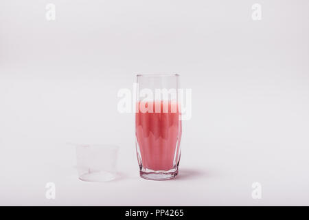 Fresche fatte sports nutrition drink. Bicchiere di rosa di proteina di siero di latte shake accanto a vuoto scoop su sfondo bianco. Foto Stock