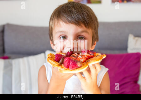 Dolce ragazzo di compleanno, mangiare i waffle belgi con fragole e lamponi e il cioccolato a casa