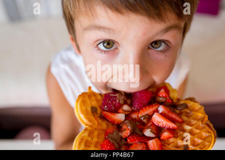 Dolce ragazzo di compleanno, mangiare i waffle belgi con fragole e lamponi e il cioccolato a casa