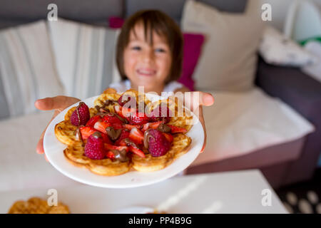 Dolce ragazzo di compleanno, mangiare i waffle belgi con fragole e lamponi e il cioccolato a casa