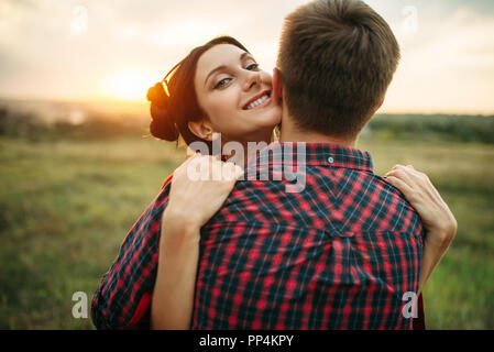 Amore giovane abbracci insieme sul prato al tramonto. Giuncata romantica di un uomo e di una donna, picnic nel campo Foto Stock