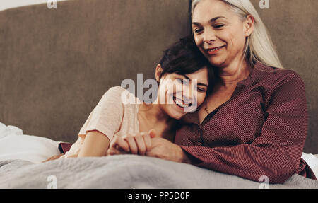 Felice la figlia e la madre giacente sul letto tenendo le mani. Donna sorridente con la testa sulla spalla di sua madre seduta sul letto. Foto Stock