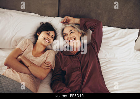 Donna sorridente dorme accanto alla sua vecchia madre sul letto con le braccia incrociate. Madre e figlia spendere tempo felice che insieme a parlare mentre giaceva sul letto a Foto Stock