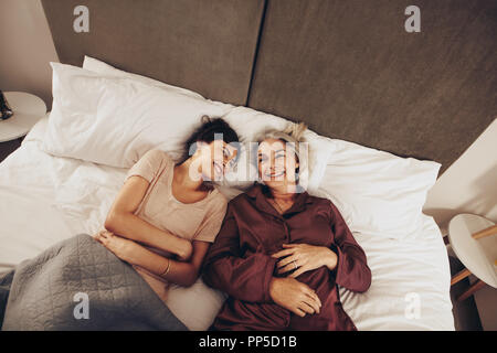 Senior donna sdraiata sul letto con sua figlia e parlare. Felice donna che dorme accanto alla sua vecchia madre sul letto con le braccia incrociate. Foto Stock