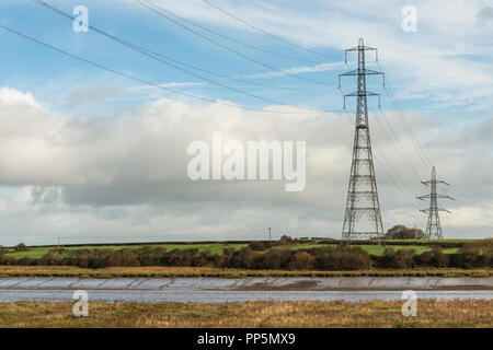 Due piloni sul lato del fiume Wyre nel Lancashire, Inghilterra, Regno Unito con i cavi ad alta tensione che attraversa il acqua nella campagna. Foto Stock