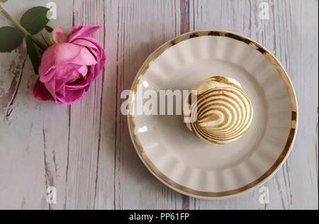 Su una piastra bianca è un delizioso marshmallow, accanto a una rosa. La vista dall'alto. Foto Stock