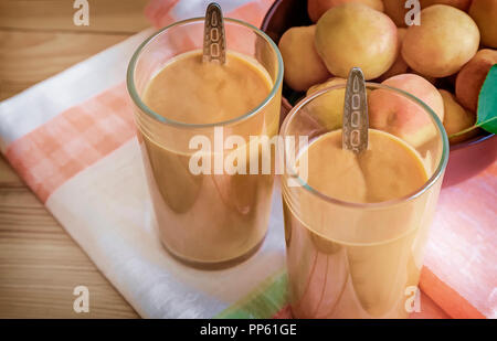 Due bicchieri di vetro con frullato di albicocche sul tavolo su un tovagliolo. Accanto alle albicocche in un vaso di vetro. Foto Stock