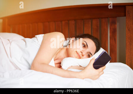 La donna posa in letto con smrtphone. Donna che guarda in telefono Foto Stock