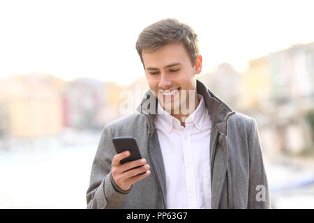 Vista frontale - Ritratto di un uomo con un telefono intelligente in inverno a piedi in una città costiera street Foto Stock