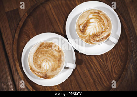 Due tazze di cappuccino sul piedistallo in legno scuro, tabella close-up vista superiore Foto Stock