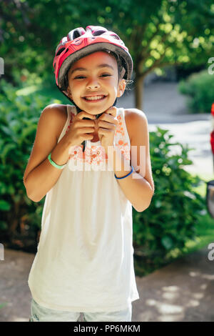 Ragazza sorridente mettendo sul casco in bici Foto Stock