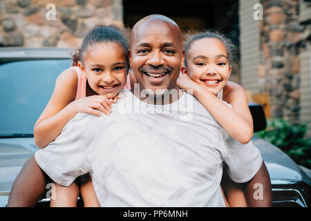 Ritratto di felice papà abbracciando le figlie di fronte a casa Foto Stock