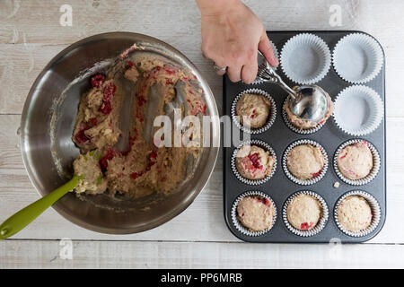 Angolo alto close up di persona il porzionamento di impasti di lampone e cioccolato bianco muffin in un vassoio da forno. Foto Stock