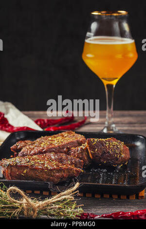 Grigliate di carne bistecche in padella e un bicchiere di birra scura su sfondo di legno Foto Stock