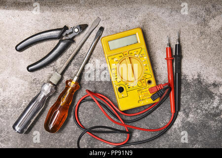 Home DIY elettricità strumenti di lavoro concetti, vecchio cacciaviti, pinze e tensione elettrica multimetro su polverosi sfondo di cemento Foto Stock