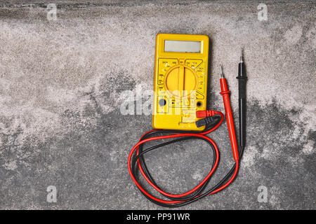 Home DIY elettricità strumenti di lavoro concetti, vecchie gialle multimetro su polverosi sfondo di cemento Foto Stock