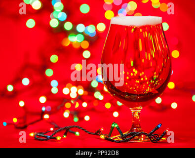 Piena snifter bicchiere di lager di birra Pilsner con le luci di Natale su sfondo rosso Foto Stock