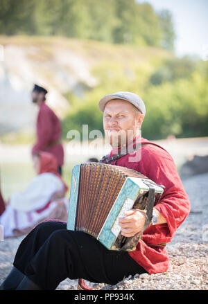 Un uomo russo in costume nazionale stand sullo sfondo di un paesaggio fantastico suonare la fisarmonica Foto Stock