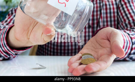 Primo piano immagine della giovane versando poche monete dal vaso di vetro con risparmio di denaro Foto Stock