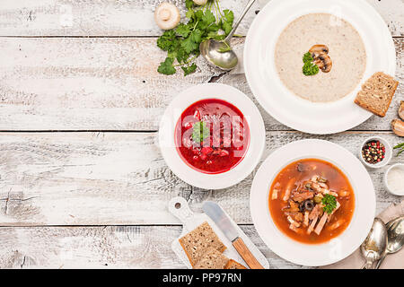 Set di tre coppe con diverse zuppe: zuppa di carne solyanka, borsh russo e funghi minestra di crema bianca su sfondo di legno, biew superiore. Foto Stock