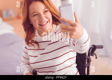 Gioiosa wheelchaired donna fare selfies Foto Stock