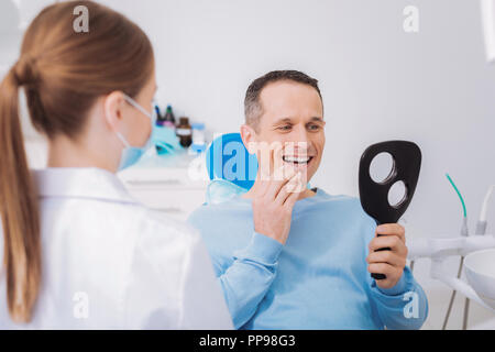 Allegro paziente guardando nello specchio e la sensazione di essere colpito dai suoi denti Foto Stock