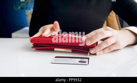 Primo piano immagine della giovane imprenditrice di prendere le carte di credito al di fuori del rosso portafoglio in pelle Foto Stock