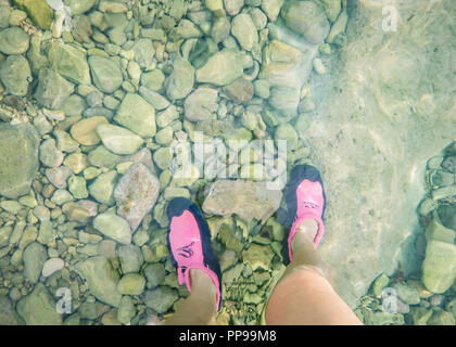 Una donna in piedi in scarpe di immersioni in acque poco profonde sulla spiaggia rocciosa, Ognina, Sicilia Foto Stock