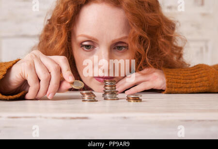 Giovane donna di risparmio di denaro in pile di monete Foto Stock