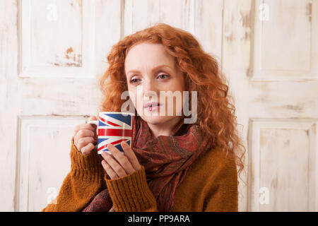 Donna che mantiene unione jack cup, cercando in questione Foto Stock