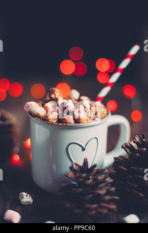 Il Natale di cioccolata calda con marshmallows su una tavola in legno rustico con pigne nelle quali luci rosse e bokeh di fondo. Messa a fuoco selettiva Foto Stock
