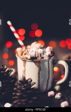 Il Natale di cioccolata calda con marshmallows su una tavola in legno rustico con pigne nelle quali luci rosse e bokeh di fondo. Messa a fuoco selettiva Foto Stock