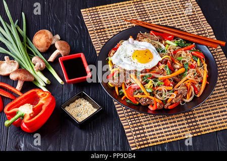 Piatto coreano Japchae: dolce fecola di patate tagliatelle saltate in padella con le verdure su una piastra nera con salsa di soia e semi di sesamo tostati, materie prime Foto Stock