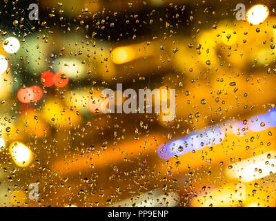 Autunno piovoso meteo - vista offuscata illuminazione urbana attraverso la finestra home con gocce di pioggia (attenzione sulle gocce di pioggia sul vetro) Foto Stock