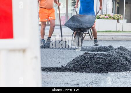 I lavoratori stradali distribuire l'asfalto caldo sulla strada con badili e carriole, Germania Foto Stock