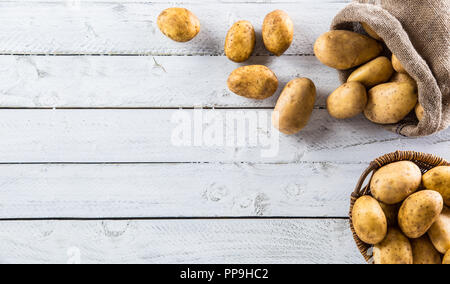 Mature le patate in una sacca di tela e cesto in legno liberamente giacente sulla tavola di legno. Foto Stock