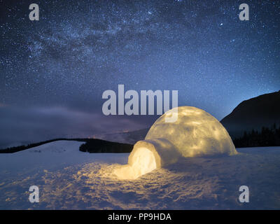 Paesaggio notturno con un igloo di neve con la luce. Casa estreme. Inverno in montagna. Il cielo con le stelle e la Via Lattea Foto Stock